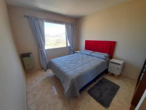 a bedroom with a bed with a red headboard and a window at Apartamentos km4 in Comodoro Rivadavia