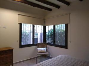 a bedroom with a bed and a chair and windows at Acogedor departamento Los Ranchos in Chacras de Coria