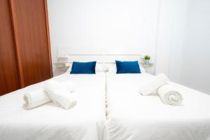 a white bed with blue pillows and towels on it at Alojamientos el Bajón in La Restinga