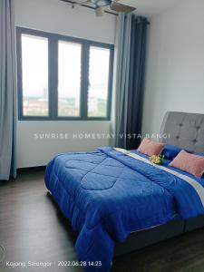 a bed with a blue comforter in a room with windows at Sunrise Homestay Vista Bangi in Kajang