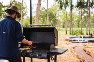 a man is cooking food on a grill at Litchfield Tropical Stay in Batchelor
