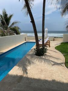 a swimming pool with two palm trees and a beach at Stunning beachfront house w/ private pool. in Zihuatanejo