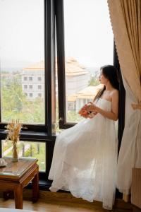 een vrouw in een trouwjurk die uit een raam kijkt bij SeaColor Beachstay Danang Hotel by Haviland in Da Nang