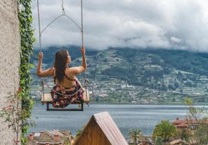 a woman sitting on a swing overlooking the water at Glamping Campo Lago San Pablo in Otavalo