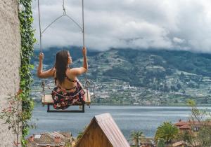 una mujer sentada en un columpio con vistas al agua en Glamping Campo Lago San Pablo, en Otavalo