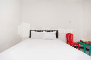 a white bedroom with a bed and a red chair at Wisma Juanda Bogor Mitra RedDoorz in Bogor