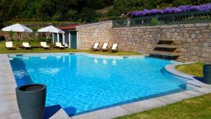 uma grande piscina azul com cadeiras e uma parede de pedra em Casas do Monte de Roques em Vila de Punhe