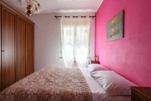 Un dormitorio con una pared de color rosa con una cama y una ventana en 3 - Casa con giardino Lotzorai - Sa Crai Apartments Sardinian Experience, en Lotzorai