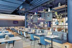 a restaurant with white tables and blue chairs at H2 Hotel München Olympiapark in Munich