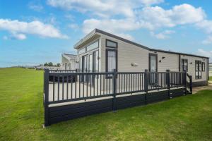 a mobile home with a black fence and grass at Stunning Caravan With Full Sea Views At Broadland Sands In Suffolk Ref 20236bs in Hopton on Sea