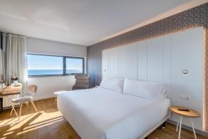a hotel room with a large white bed and a desk at Occidental Atenea Mar - Adults Only in Barcelona