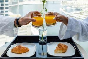 two people holding glasses of orange juice and pastries on a tray at Unlock J One Downtown Dubai in Dubai