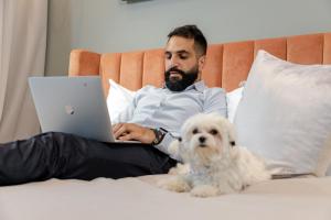 un homme assis sur un lit avec un ordinateur portable et un chien dans l'établissement Unlock J One Downtown Dubai, à Dubaï