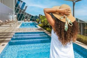 una donna con un cappello in piedi accanto alla piscina di Unlock J One Downtown Dubai a Dubai