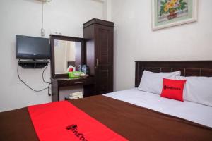 um quarto com uma cama com uma almofada vermelha e uma televisão em RedDoorz at Hotel Rich Parepare near Pantai Mattirotasi em Parepare