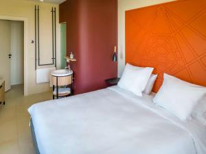 sypialnia z dużym białym łóżkiem z pomarańczowym zagłówkiem w obiekcie Ibis Styles Mayotte Aéroport w mieście Pamandzi