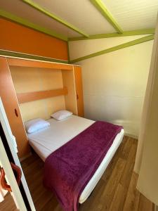 ein kleines Schlafzimmer mit einem Bett mit einer lila Decke in der Unterkunft Le Camping de la Plage in Aregno