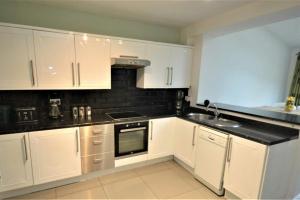 een keuken met witte kasten en een zwart aanrecht bij Lovely 3 bedroom house in Romiley, Stockport with parking for 3 cars in Romiley