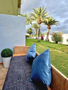 Stunning lovely flat with Pool and strong Wi-Fi في أرونا: اثنين من الوسائد الزرقاء جالسين على مقعد مع أشجار النخيل
