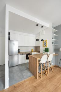 ワルシャワにあるObrzeżna Comfort Apartmentの白いキャビネット、木製テーブルと椅子付きのキッチンが備わります。