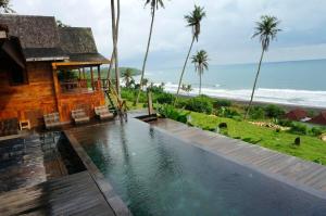a swimming pool in front of a house next to the ocean at 4 bedrooms villa with sea view private pool and furnished garden at Kabupaten de Tabanan in Antasari