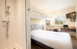 a hotel room with a white bed and a shower at Ibis Budget Fréjus Capitou in Fréjus
