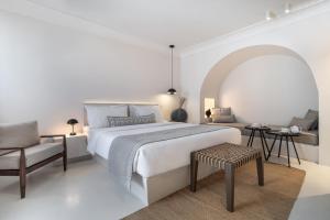 um quarto branco com uma cama grande e uma cadeira em Akra Suites & Spa em Imerovigli