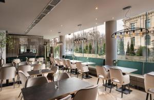 un restaurante con mesas, sillas y ventanas en Leonardo Hotel Bucharest City Center, en Bucarest
