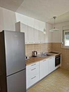 La cuisine est équipée de placards blancs et d'un réfrigérateur en acier inoxydable. dans l'établissement Apartment Melody, à Metković