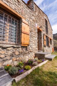 un edificio de piedra con una ventana y algunas flores en Casa rústica la Borda de la Munda., en Arsèguel