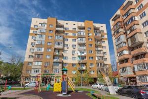 un gran edificio de apartamentos con un parque infantil delante de él en Светлая квартира рядом с парком Горького, en Almaty