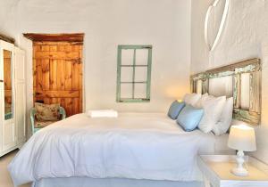 a white bedroom with a large white bed with blue pillows at Brakdakkie Guest Cottages in Prince Albert