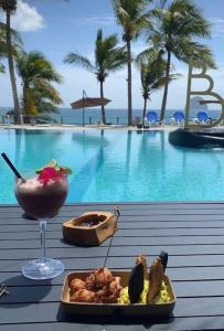 a drink and a plate of food next to a pool at Appartement terrasse vue mer et piscine in Le Diamant