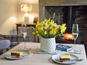 a table with a vase of yellow flowers and wine glasses at Fern Cottage in Bardon Mill
