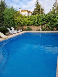 a large blue swimming pool with two chairs and a house at Casa cerca de Sevilla con piscina in Valencina de la Concepción