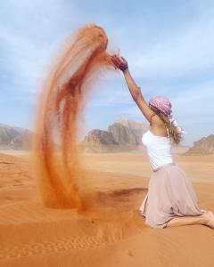 a woman sitting in the desert with her hand in the air at Experience sleep under the star in Wadi Rum