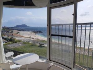 a view of the beach from a room with a table and chairs at White Castle Pension in Jeju