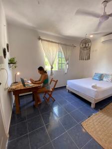 a woman sitting at a desk with a laptop in a bedroom at Barco Verde Hostel in Holbox Island