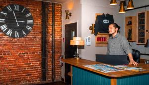 a man standing at a table with a clock on the wall at The Cambie Hostel Seymour in Vancouver