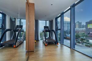 a gym with treadmills in a building with windows at Dongguan Tangxia Huaman Hotel in Dongguan