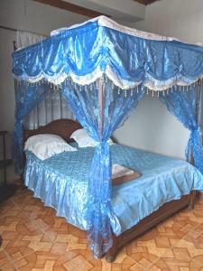 una cama cubierta de cortinas azules en una habitación en TAMATAVE Chez Bien Aimée, en Toamasina