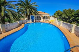 a large blue swimming pool on a deck with palm trees at NEO - sea view villa with private pool in Moraira in Teulada