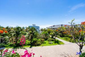 um jardim com flores e palmeiras e um edifício em MIA Beach Villa - Oceanami Resort Long Hai Vung Tau em Long Hai