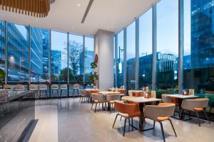 a restaurant with tables and chairs and large windows at UrCove by HYATT Nanjing South Railway Station in Nanjing