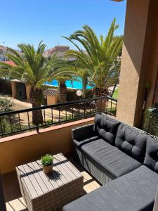 einen Balkon mit einem Sofa, einem Tisch und Palmen in der Unterkunft Apartamento ESTRELLA con vistas a la piscina in Torrevieja