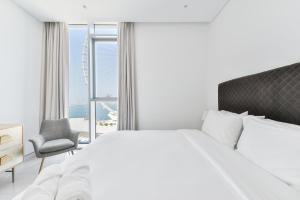 a white bedroom with a large bed and a chair at Spectacular 3 BR condo with maids room facing the Dubai Eye in Dubai