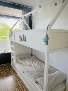 Ce lit superposé blanc se trouve dans un dortoir doté d'une fenêtre. dans l'établissement PANORAMIC FeWo SEESCHWALBE - Pool - Familien - strandnah - Hunde, à Sierksdorf
