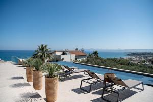 uitzicht op een zwembad met stoelen en de oceaan bij AGAVE HILL LUXURY HOUSE in Chania