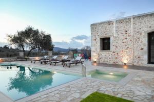a swimming pool with chairs and a stone house at Heliopetra Lux Villa with private Pool in Varípetron