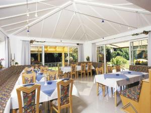 un restaurante con mesas y sillas blancas y ventanas en Gästehaus Brütting, 